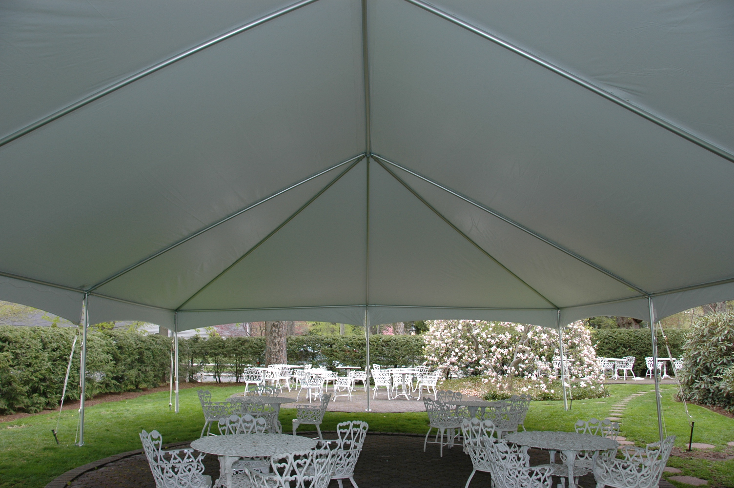 Bright clear-span frame tent set up over an outdoor patio with furniture